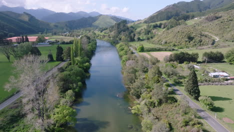 drone shot over silver car driving along highway next to motueka river, new zealand