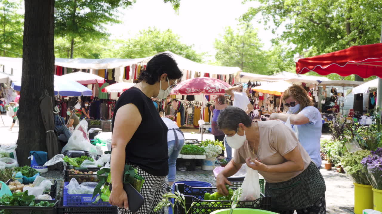 Medium shot of a woman buying vegetables to a farmer, while wearing masks in a fair, after the end of lockdown (deconfinement), in Barcelos, Portugal.