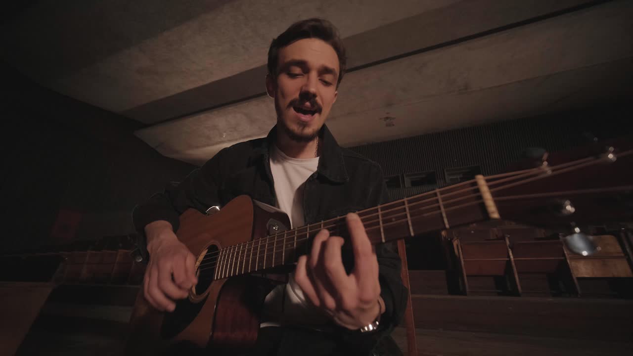 un chico guapo toca una guitarra acústica en un cine abandonado. el músico canta una canción y acompaña en la guitarra