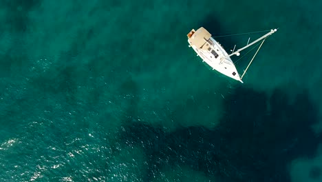 vista aérea de arriba hacia abajo de un velero anclado en aguas azules transparentes