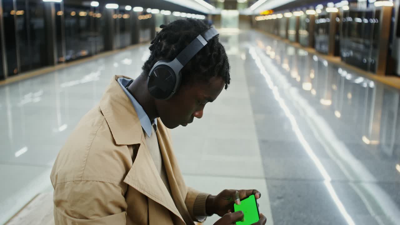Man with Headphones Using Phone with Green Screen in Subway
