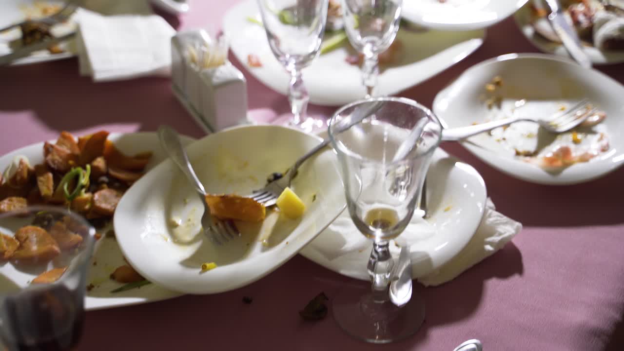 dirty plates and cutlery with wineglasses are located on a pink tablecloth. Camera motion forward