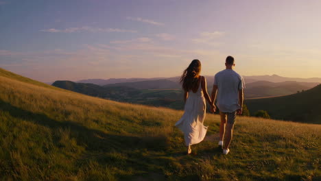 couple walking hand-in-hand on a grassy hill at sunset