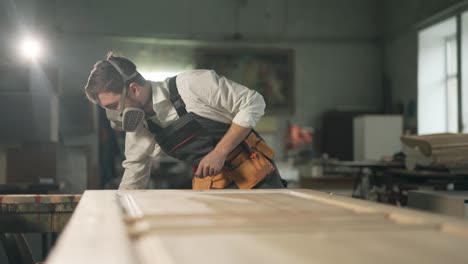 A-handsome-man-in-the-form-of-a-painter-in-a-protective-respirator-paints-a-wooden-product-with-a-brush