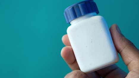 hand holding a white plastic bottle with a blue lid