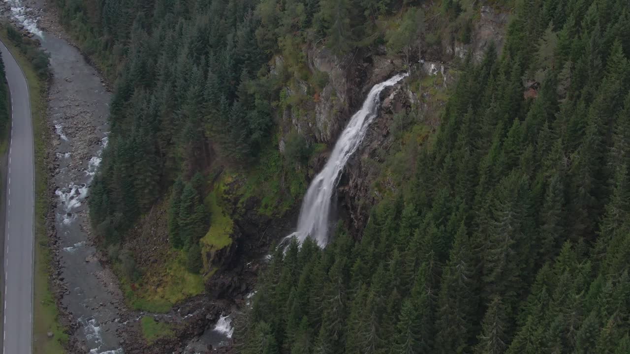 una cascada desciende por una ladera de montaña llena de árboles a un camino sinuoso en el desierto de noruega