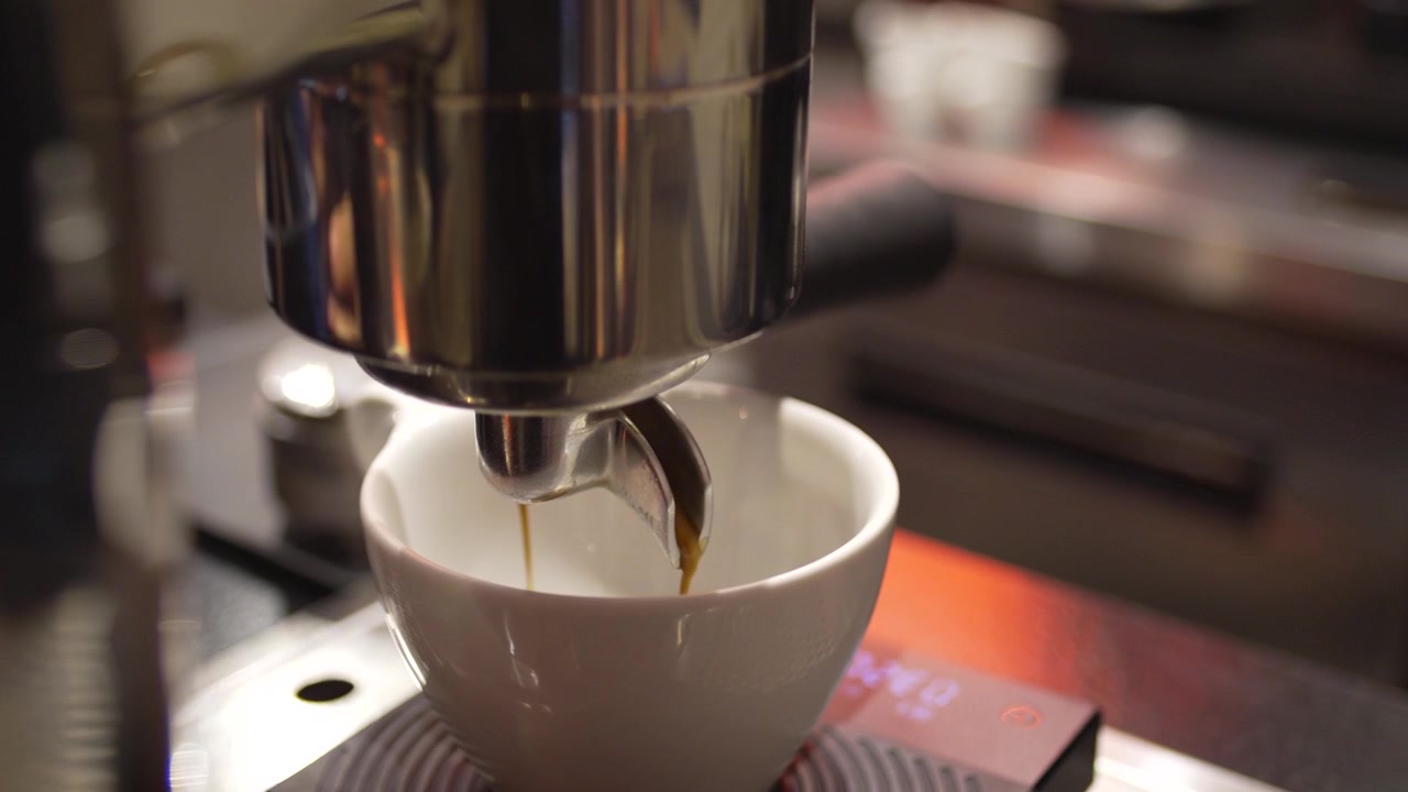 Primo piano della preparazione di un espresso artigianale, tazza bianca in una moderna caffetteria specializzata.