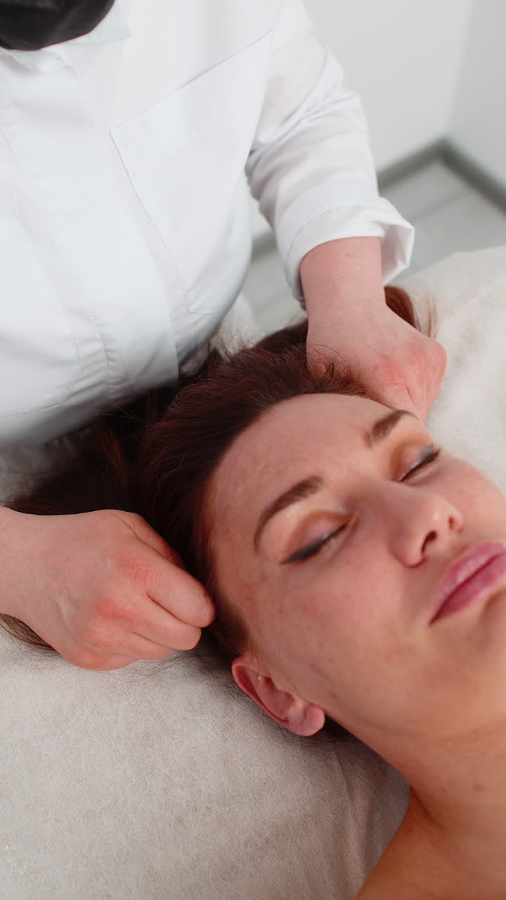 Mujer recibiendo un masaje capilar en una clínica de cosmetología por una esteticista durante un procedimiento terapéutico de relajación