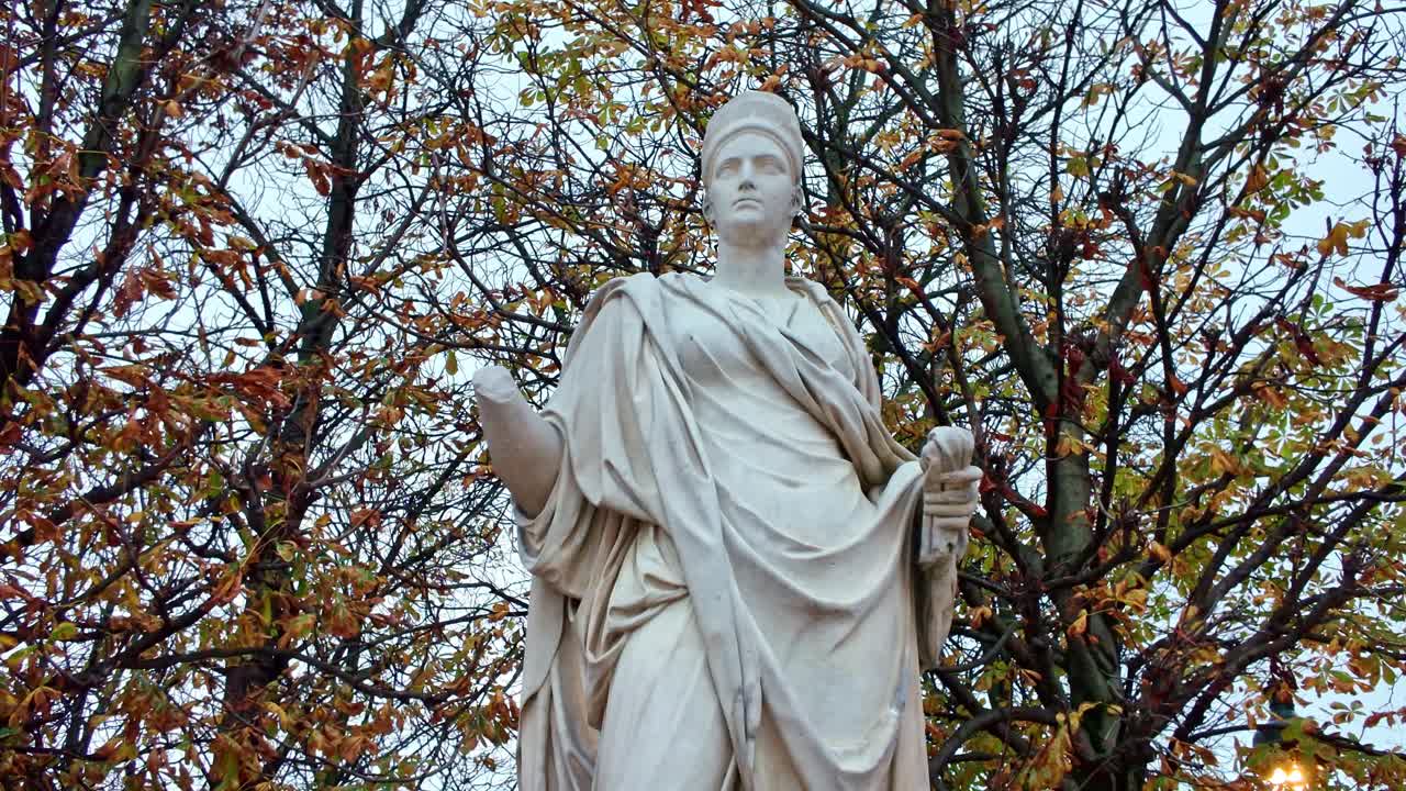 Svelatura verticale dall'alto verso il basso, inclinata verso l'alto, della statua di Agrippina di Robert Doisy, che rivela drappeggi neoclassici in marmo sullo sfondo del fogliame autunnale nel Jardin des Tuileries, nel 1° arrondissement di Parigi
