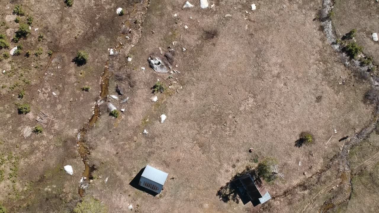 drone vuela sobre pradera con cabañas y arroyos serpenteantes mirando hacia abajo