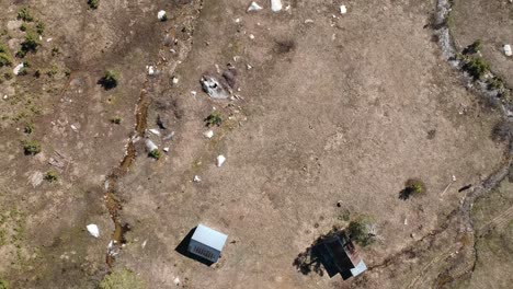 Drone-flies-over-meadow-with-cabins-and-meandering-streams-looking-down