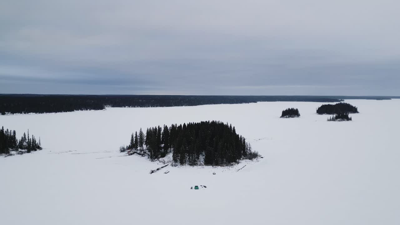 An outdoor Drone Shot of an Island on Frozen Canadian Paint Lake with an Ice fishing hut and skioos