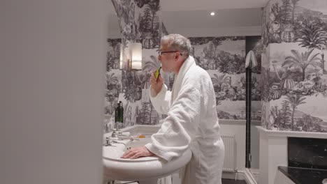 Man-wearing-dressing-gown-has-a-dry-shave-in-a-bathroom,-locked-off