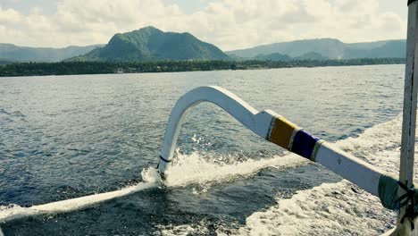 a traditional outrigger boat sailing on blue waters with a mountainous island landscape in the background