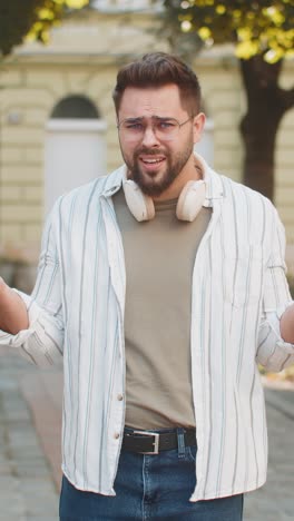 doubtful sad frustrated young caucasian man shrugging shoulders dont know answer on city street