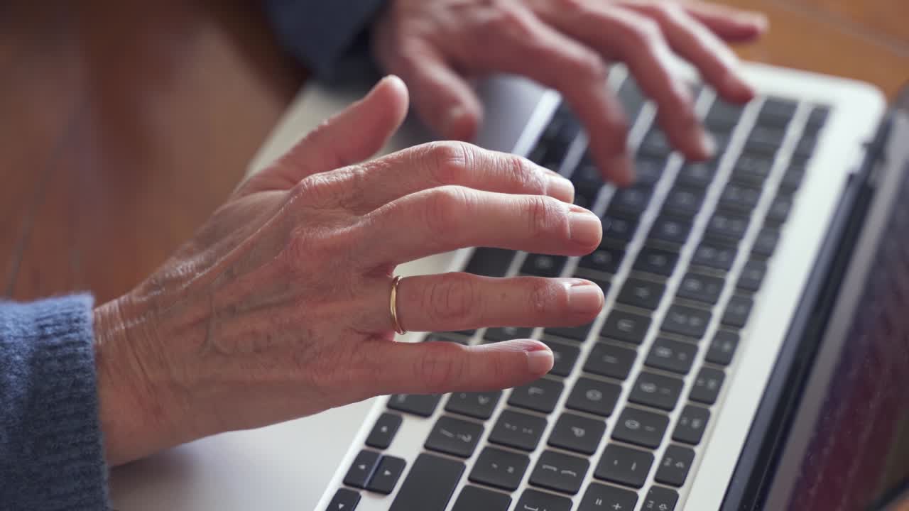 manos arrugadas de una anciana con anillo de oro usando una computadora portátil