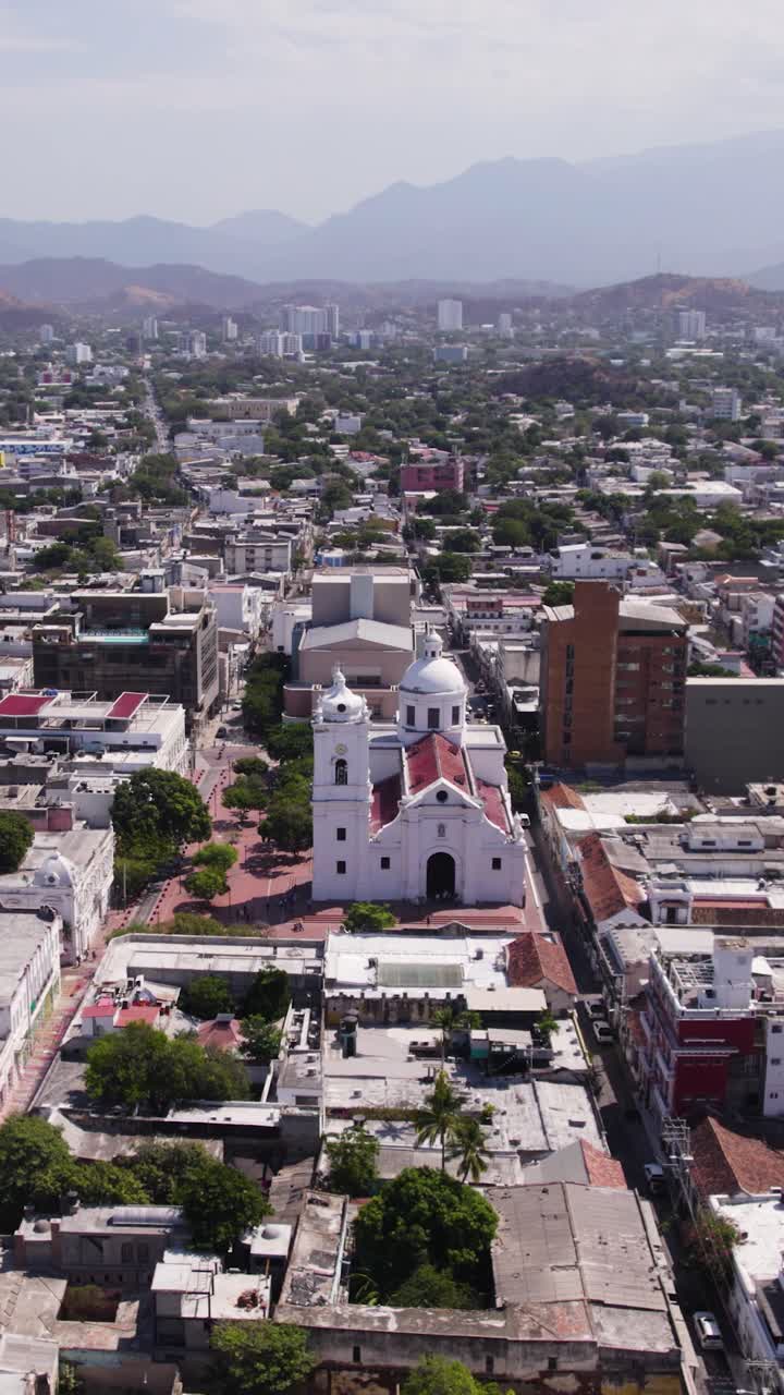 Aerial view of the Cathedral Basilica of Santa Marta surrounded by urban buildings in Santa Marta, Colombia. Vertical Video, Push Forward Shot