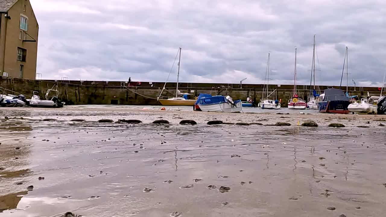 A view of boats and buoys resting on a sandy shoreline with a cloudy sky overhead.