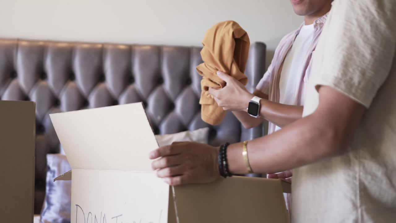 African American men packing orange garment into box labeled DONATIONS! on bed for donation