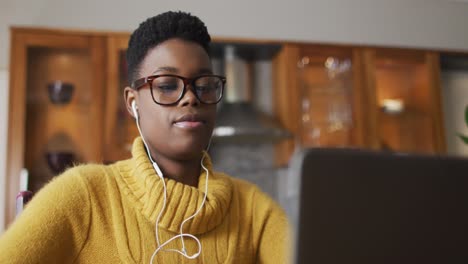 african american woman wearing earphones using laptop while working from home