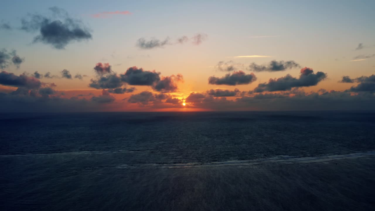 Wunderschöne Drohnenaufnahme eines ruhigen Sonnenaufgangs über dem Meer am Well Beach bei João Pessoa an einem warmen Sommermorgen, mit dem Wasser darunter und goldenen Wolken am Horizont.
