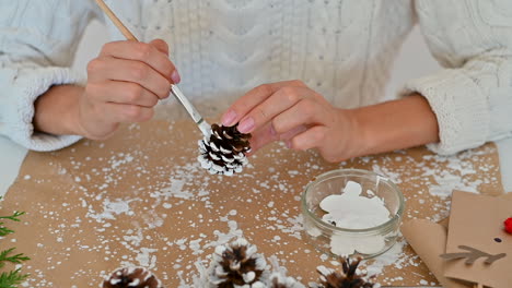 woman hands decorate pine cones with white paint for christmas