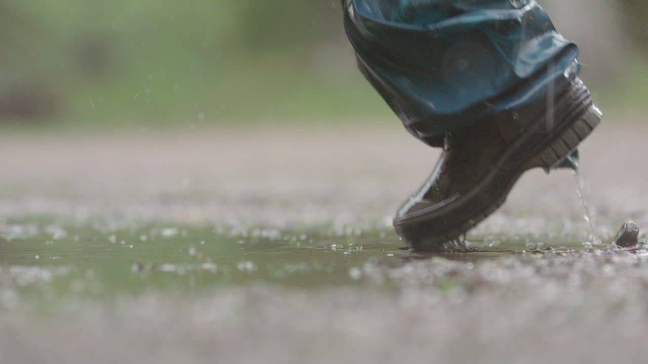 SLOW MOTION, CLOSEUP - A child jumping in the puddle during heavy rain
