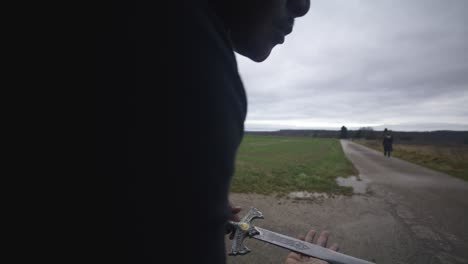 Modern-Black-Swordsman-Warrior-Awaiting-Battle-Opponent-in-Open-Field-Under-Grey-Sky,-Europe,-4K-|-Muscular,-Intimidating,-Shadow,-Figure,-Blurry,-Dark-Clothes,-Powerful,-Criminal,-Close-Up,-Traveler