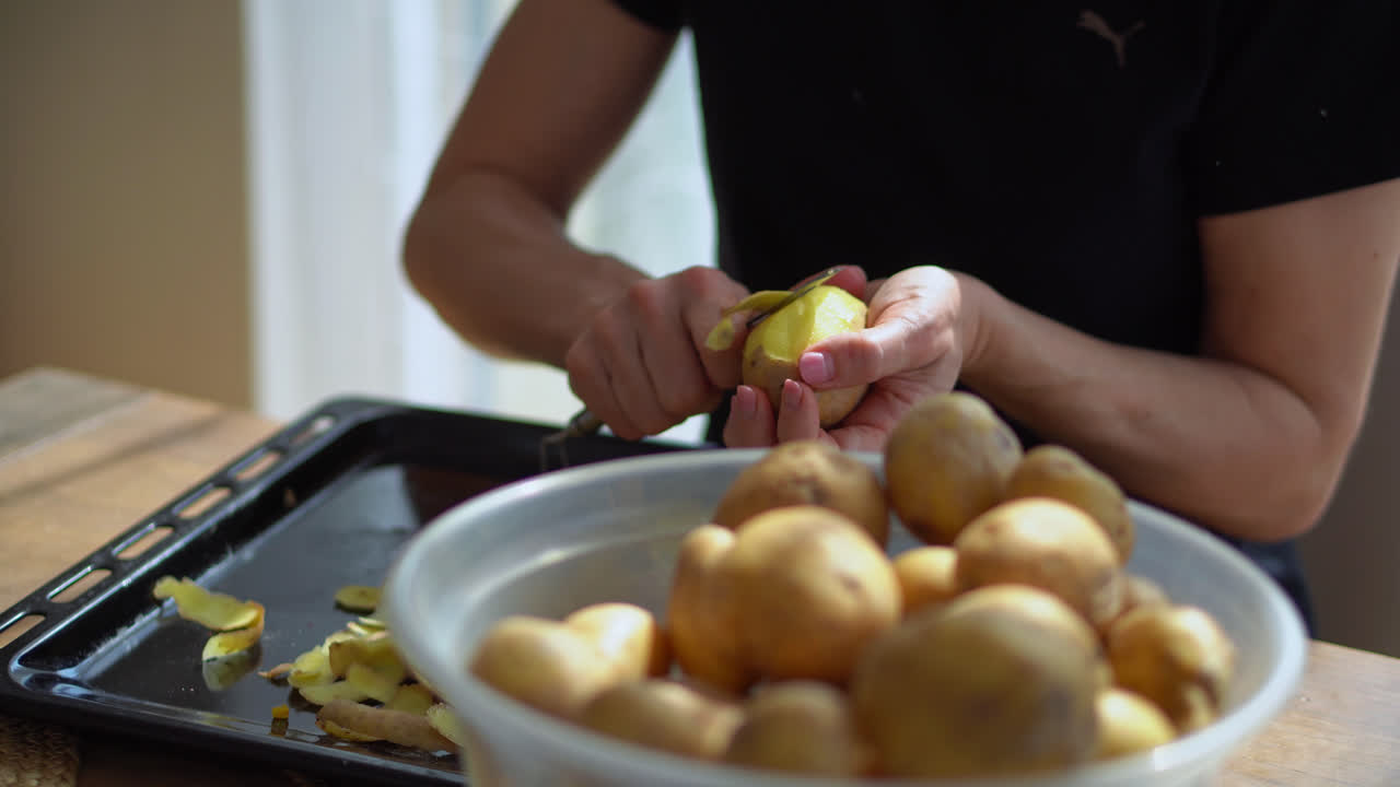 mano de una mujer recogiendo patatas crudas de un recipiente de plástico para pelarlas con un pelador