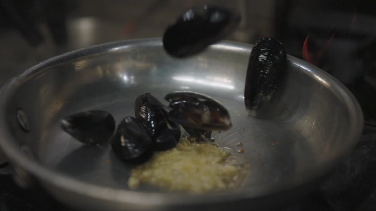 Fresh mussels simmer in a flaming pan, releasing savory juices and aroma