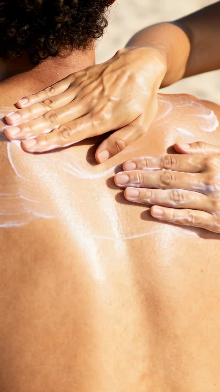 Vertical video: Therapist starting dotted cream then rubbing hands across sunlit back for skincare