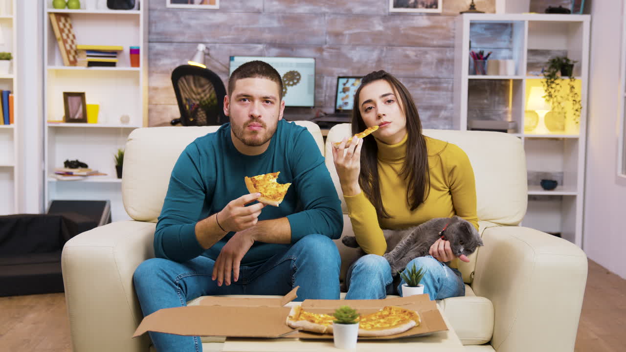 Coppia che mangia pizza e guarda la TV con il proprio gatto