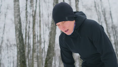 A-young-man-on-a-morning-jog-in-the-winter-forest-was-tired-and-stopped-to-rest-and-ran-on.-He-recovered-his-strength-and-overcame-fatigue-and-continued-to-run.-Perseverance-and-overcoming-weakness.-Striving-forward.-Slow-motion.-Healthy-lifestyle