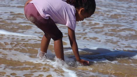 slow motion close up shot of a little girl bending over and running her hands through the water on the coastline