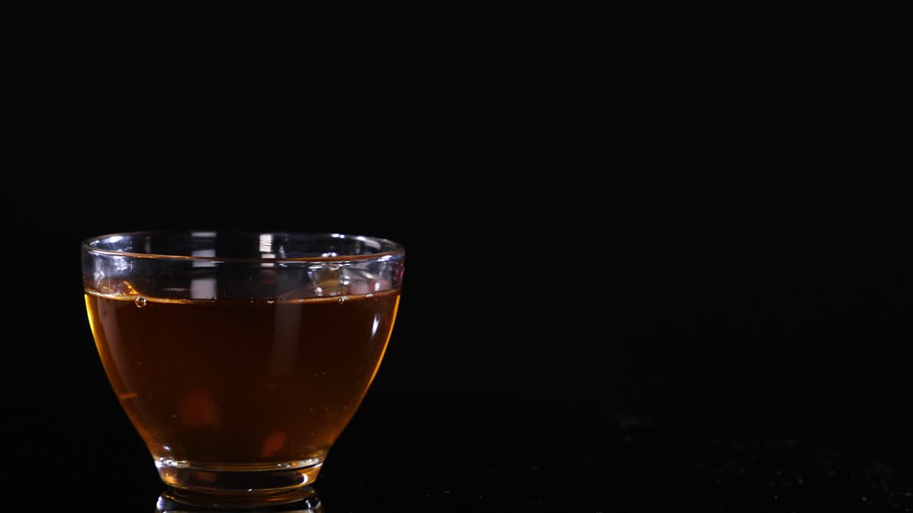A glass cup filled with tea sits on a black background, highlighting its warm color and transparency