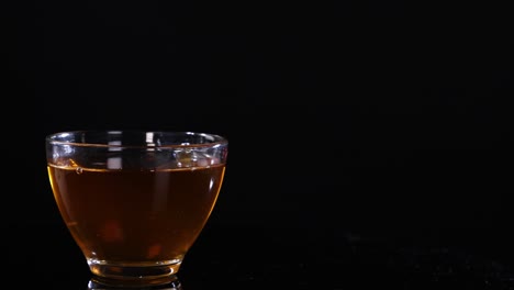 a glass cup filled with tea sits on a black background, highlighting its warm color and transparency