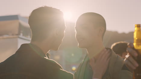 young homosexual couple kissing enjoying rooftop party at sunset dancing together sharing intimate connection group of friends having fun celebrating summer vacation