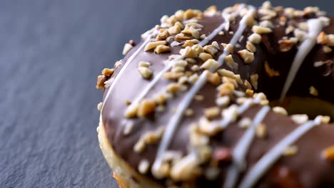 close-up half-shot of glazed brown donut with crushed nuts and white topping spinning slowly on gray table background.