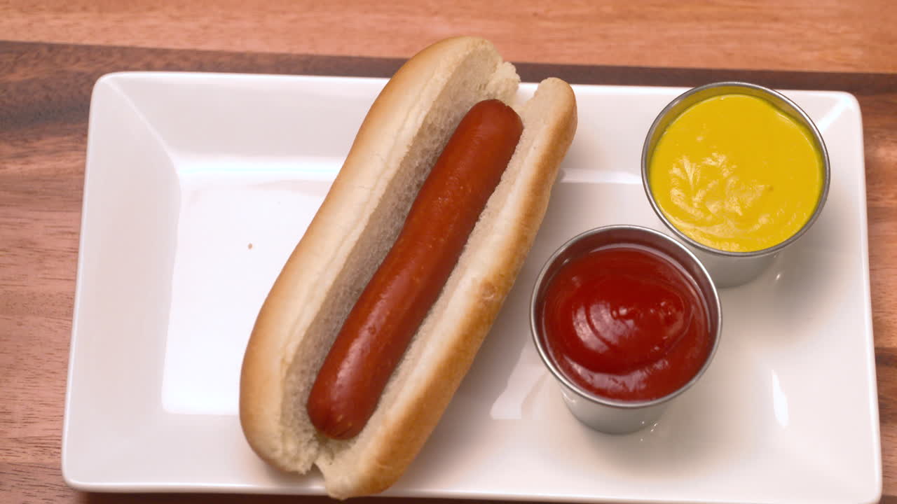 Bovenaanzicht van een hand die een hotdog van een bord pakt.