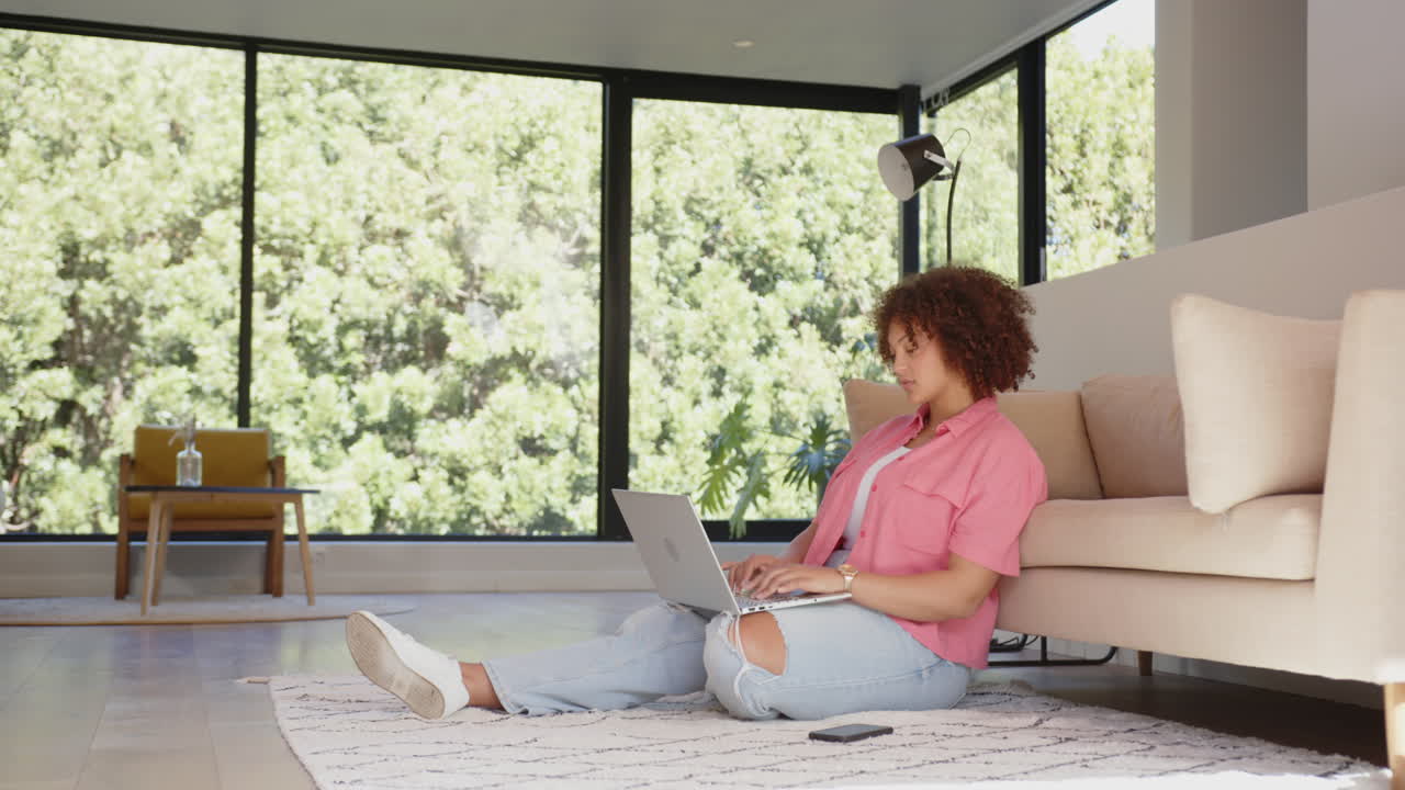 Sitting on floor, woman using laptop and smartphone in modern living room, copy space