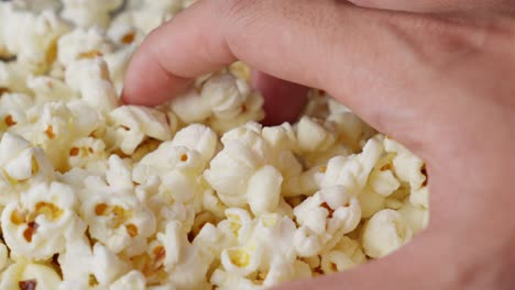 Hand-grabbing-tasty-salted-popcorn-snacks-in-closeup