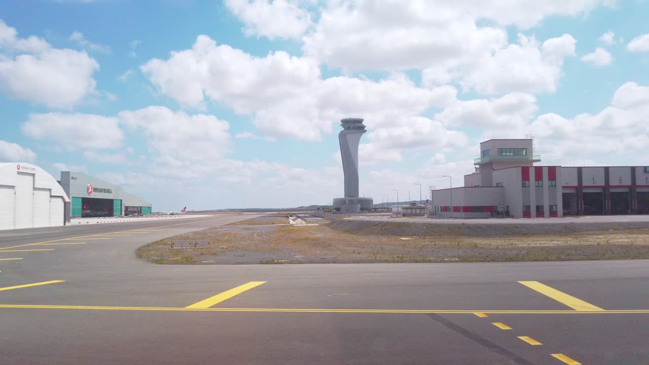 On a partly cloudy day, a daytime view captures Istanbul Airport's fire station, the Turkish Technic aircraft maintenance facility behind it, and the iconic Istanbul Airport control tower