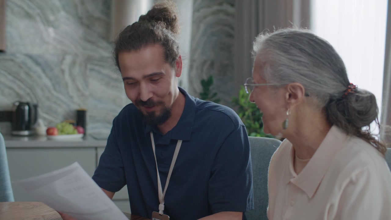 Assistente sociale che spiega un documento finanziario a una donna anziana durante una visita a domicilio