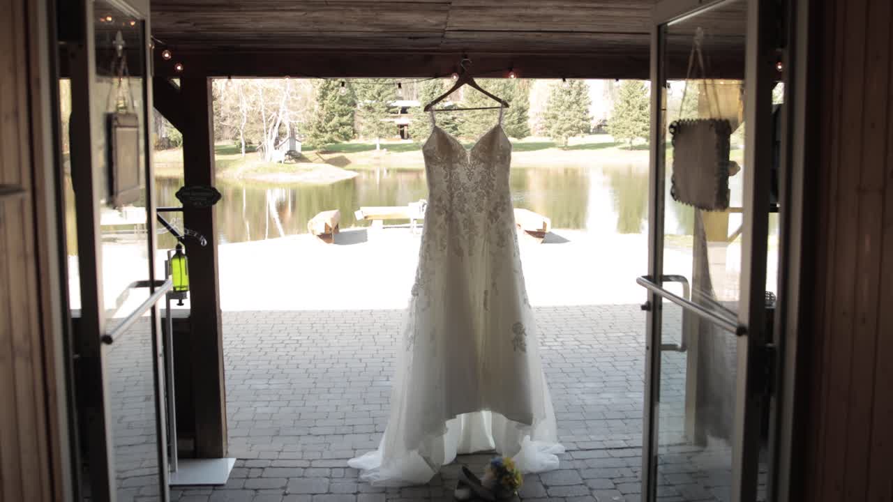 Walking out of a rustic wedding venue with a elegant wedding dress hanging just outside the entrance way with a pond and trees in the background at Bean Town Ranch near Ottawa Canada