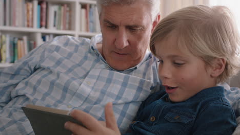 Abuelo-Mostrando-A-Un-Niño-Cómo-Usar-Una-Tableta-Enseñando-A-Un-Nieto-Curioso-Tecnología-Moderna-Dispositivo-Móvil-Inteligente-De-Aprendizaje-Infantil-Sentado-Con-El-Abuelo-En-El-Sofá-4k