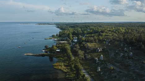 aerial shot over a small costal community next to rauk stones with wind power plants in the distance