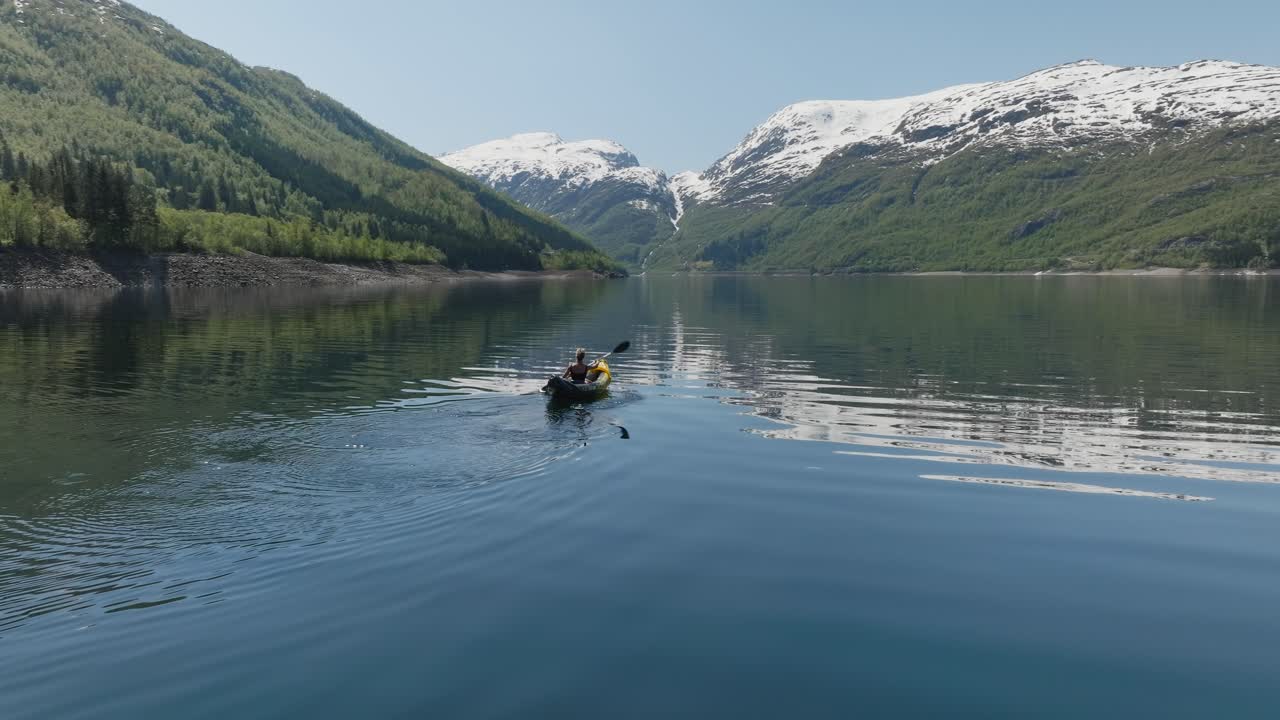 Un Kayakista Pagaia su un Tranquillo Lago Norvegese Circondato da Montagne Innevate in una Giornata Limpida