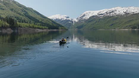 Kayaker-paddles-on-calm-Norwegian-lake-surrounded-by-snow-capped-mountains-on-a-clear-day