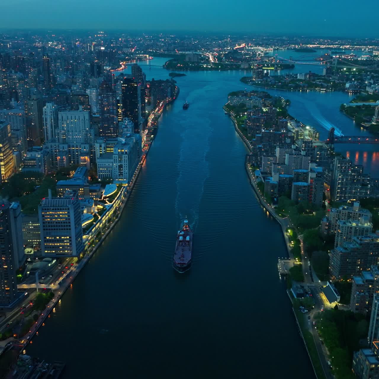 Big boat slowly moving by the dark blue river and approaching Queensboro bridge. Amazing New York cityscape with billions of lights. Aerial view