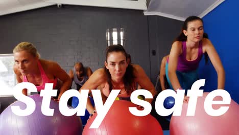 Animation-os-stay-safe-text-over-people-exercising-with-swiss-balls-in-fitness-class